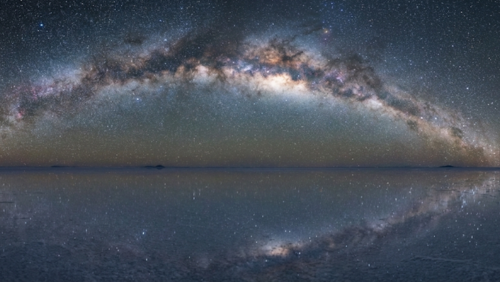 夜のウユニ塩湖。湖面に星空が鏡のように映り込み、天の川もはっきり見える幻想的な風景。