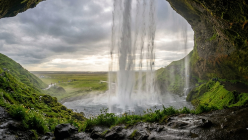 セリャラントスフォス滝を裏側から眺めた幻想的な風景。緑の崖と水しぶきが広がる。