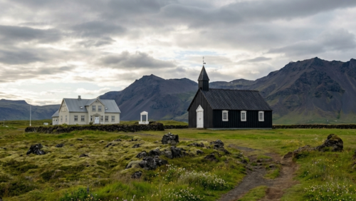 Hótel Búðir周辺の古い黒い木造教会と緑の草原、背景に山と溶岩原が広がる風景
