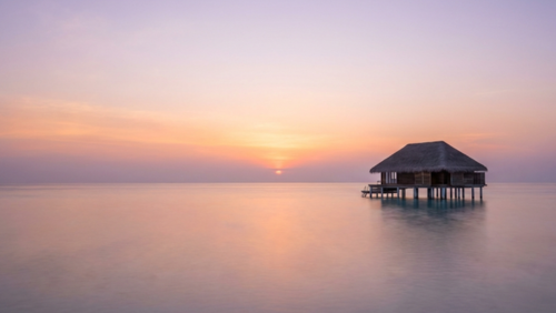 夕暮れのモルディブ。広い海の上に一棟だけ建つ水上ヴィラが静かに佇む風景
