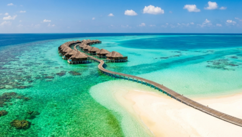 ターコイズブルーの海と一直線に伸びる桟橋、水上ヴィラが並ぶモルディブの空撮風景