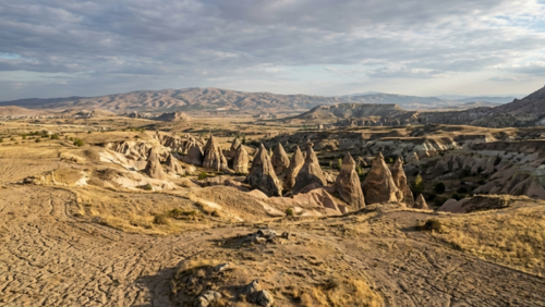 トルコ中央部のアナトリア高原の中に位置するカッパドキアの奇岩群の風景。広大な高原の草原の中に円錐形の岩が点在し、地形のつながりがわかる景観。