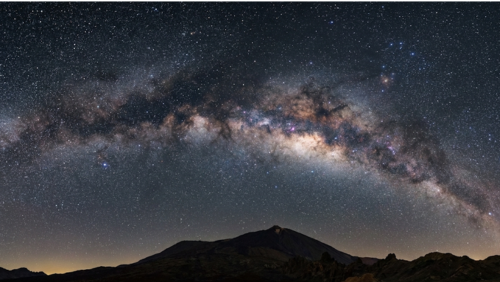 カナリア諸島の高地とテイデ山周辺の夜景。天の川が輝く満天の星空と火山地形のシルエットが広がる。
