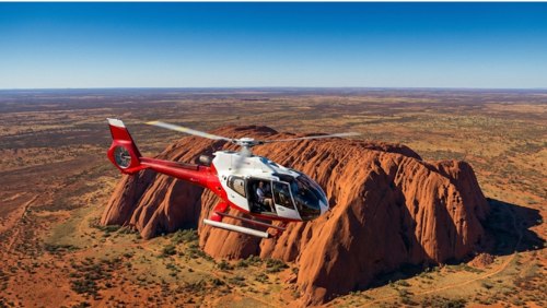 ウルル上空を飛行する観光用ヘリコプターと、眼下に広がる巨大な一枚岩と赤い砂漠の風景