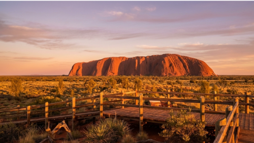 オーストラリア中央部の木製サンセット展望台から見たウルル、夕日の黄金色に染まる赤い砂漠と岩山
