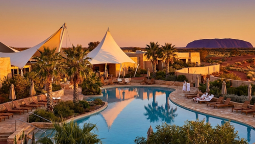 ウルル近郊の高級ホテル「セイルズ・イン・ザ・デザート」の帆の形をした建物とプール、赤砂漠に囲まれたラグジュアリーなリゾート風景