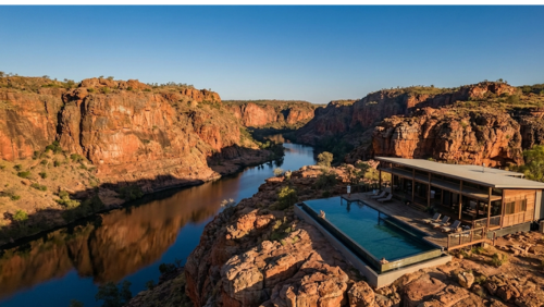 オーストラリア・ニトミルク渓谷の赤い砂岩の断崖に寄り添うように建つ、高級エコロッジ「シケイダ・ロッジ」。上空から見下ろす視点で、自然と調和した木造建築のロッジやインフィニティプール越しに、何万年もかけて削られた重厚な渓谷と眼下を流れる静かな川が広がる、圧倒的なスケールと特別感を感じさせる風景写真
