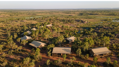 アーネムランドの手つかずの自然の中に点在する、「デビッドソンズ・アーネムランド・サファリ」の宿泊施設を上空から捉えた風景。ユーカリの木々と赤土の大地に溶け込むようにゆったりと配置された木造キャビンの奥には、地平線まで続く果てしないサバンナと湿地帯が広がっている。