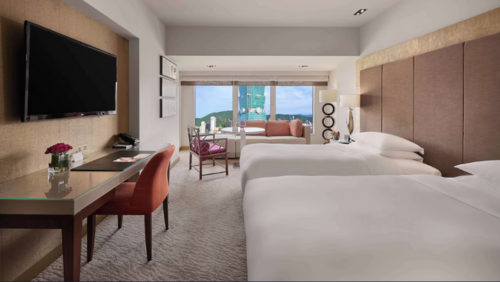台北101を正面に望むグランド ハイアット 台北の客室。清潔感のある2台のシングルベッド、壁掛けテレビ、広々としたワークデスク、奥の窓際には外を眺められるソファセットが配置されたモダンで落ち着いた雰囲気の部屋
