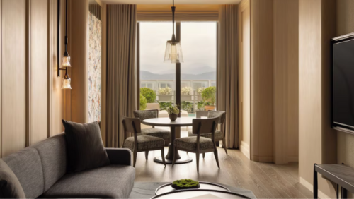 カペラ台北の客室。イタリアのフレッテ製シーツを使用した高級寝具のベッド、室内セーフティボックス、無料アイテムを備えたミニバーなど、充実した設備が整う。大きな窓からはテラスの緑と台北の景色が広がり、洗練されたインテリアとともに上質な滞在を演出する空間。