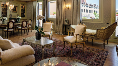 バリョーニ ホテル ルナの豪華なスイートルーム。ヴェネツィアの伝統的な様式のアンティーク家具、精緻な装飾が施されたソファ、重厚なペルシャ絨毯が配され、大きな窓からは明るい自然光が差し込む気品あふれる室内空間