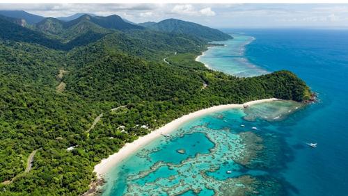 クイーンズランド州、デインツリー熱帯雨林の深い緑がケープ・トリビュレーションの白い砂浜へと続き、そのままエメラルドグリーンのグレートバリアリーフへと溶け込む絶景の空撮写真。太古の森と世界最大のサンゴ礁という2つの世界遺産が直接出会う、地球上で唯一の場所を捉えている。透明度の高い海には複雑なサンゴ礁の模様が浮かび上がり、海岸線に沿って熱帯の山々が地平線まで連なっている