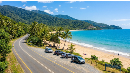 キャプテンクック・ハイウェイ沿いのエリス・ビーチ。道路のすぐ脇に広がる白い砂浜とパームツリー、路肩に停車した車が並ぶ南国ドライブの風景