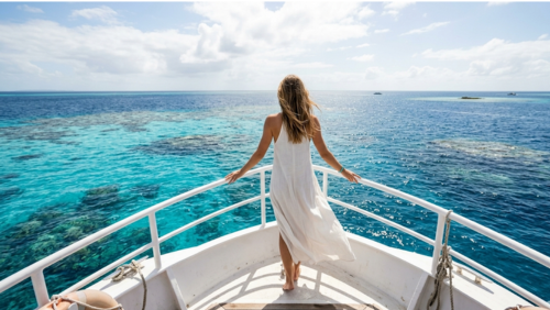 ボートのデッキに立ち、ターコイズブルーからコバルトブルーへと広がるグレートバリアリーフの海を眺める女性の後ろ姿