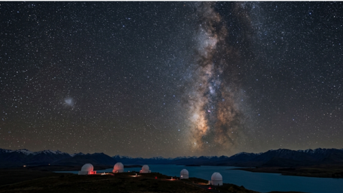 マウントジョン天文台の夜空。白い観測ドームの上に無数の星が広がり、天の川とともに大マゼラン雲と小マゼラン雲が肉眼でも分かるほど明るく浮かび上がる、圧倒的なスケールの星空。