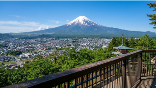 日本語: 展望デッキから見た新倉山浅間公園の絶景。眼下に広がる富士吉田市の街並みと、その先に雄大にそびえる富士山、そして手前には五重塔が見える晴れた日の風景。
英語: A breathtaking panoramic view of Mount Fuji and the Chureito Pagoda seen from the observation deck at Arakurayama Sengen Park, overlooking the city of Fujiyoshida under a clear blue sky.