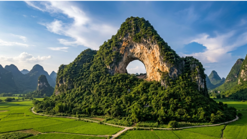 中国・陽朔にある月亮山。山の中央に大きな月形の天然アーチが開いた特徴的なカルスト地形で、緑豊かな田園風景の中にそびえ立つ桂林屈指の絶景スポット。青空を背景にした自然の芸術作品のような風景。